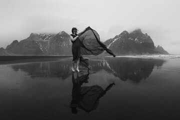 Woman in dress with waving cape on beach monochrome scenic photography. Picture of person with hills on background. High quality wallpaper. Photo concept for ads, travel blog, magazine, article