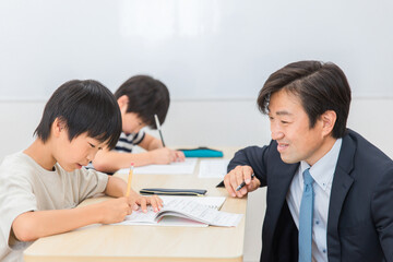 小学生に授業で勉強を教える笑顔の塾講師・先生（夏期講習・日本人男性）
