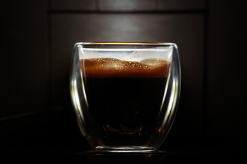 Foam layer of an espresso coffee in a double-walled glass cup against dark background. Coffee industry concept close up photo.