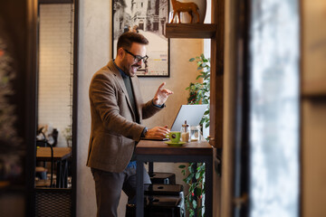 Fototapeta na wymiar Handsome young businessman with glasses, using a laptop and a smart phone while working in the cafe