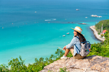 Asian woman with backpack travel at tropical island and resting on mountain peak in summer sunny...