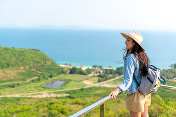 Asian woman with backpack solo travel on tropical island mountain peak in summer sunny day. Attractive girl enjoy and fun outdoor lifestyle looking beautiful nature of ocean on beach holiday vacation.