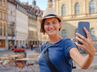 summer female solo trip to Europe, happy young woman walking on european street, on the town building background in Munich. making pictures or selfie on the sunny day.