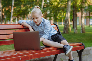 Fototapeta na wymiar cute caucasian boy sitting on bench in park with laptop computer. Black screen