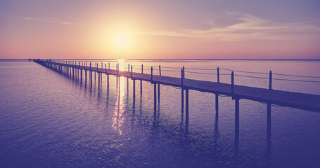 Fototapeta na wymiar Wooden pier silhouette at sunrise, color toning applied.