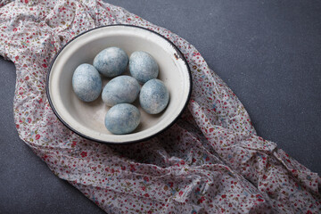 Easter eggs DIY painted blue in white bowl on grey wooden background with kitchen towel. Copy space