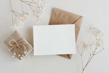 Greeting card mockup, envelope, gift box and  dried gypsophila flowers twigs on white background top view flatlay. Card mockup with copy space.