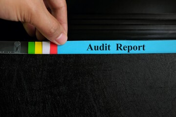 Hand picking audit report file record in black binder folder. Auditing in company organization concept.