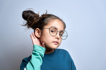 Fototapeta premium Little caucasian girl holds hand near ear, listening carefully, hearing intently isolated on white background