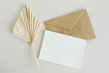 Greeting card mockup, envelope and  dried palm leaf on beige background top view flatlay. Card...