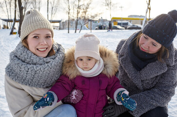 Grandmother, mother and daughter are walking in the winter city park on Christmas and New Year holidays. Parent and little child having fun outdoors