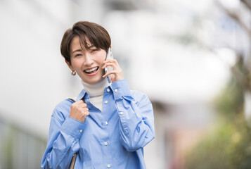 携帯電話で話ながら街を歩く笑顔のアジア人女性	