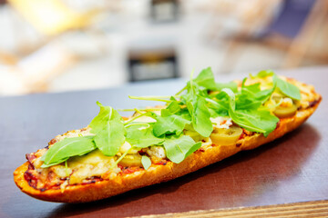 baguette with tomato sauce, meat, jalapeno and arugula baked with cheese on a table outdoor