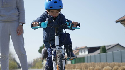 Little boy learning to ride bicycle outside in green pathway during winter season. Child learns to bike outdoors