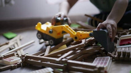 Kid plays with bulldozer tractor toy picking pieces of wood playing at home playroom. Closeup child hands