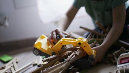 Kid plays with bulldozer tractor toy picking pieces of wood playing at home playroom. Closeup child hands