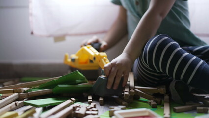 Kid plays with bulldozer tractor toy picking pieces of wood playing at home playroom. Closeup child hands