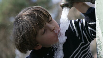 Obraz premium Closeup of flowing water faucet child hand and mouth drinking outdoors at public park. One little boy hydrating himself