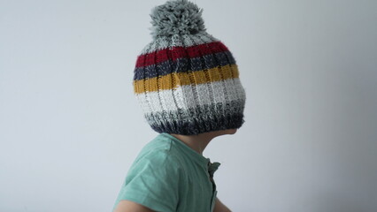 Child face covered with beanie hat. Funny playful little boy blind by knit wool winter accessory