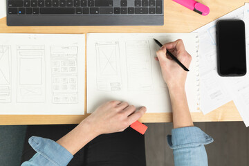 Sketch of wireframe for website. Women designer working on a mobile application, drawing on paper.