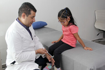 Latino doctor medic and girl patient in medical office checks her reflexes on hammer in her checkup...