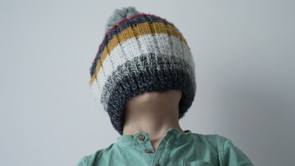 One little boy putting beanie covering face. Funny child wearing wool winter clothing accessory