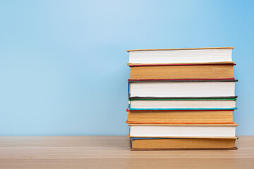 Stack of books in the colored cover lay on the wooden  table and blue backround. Education learning concept