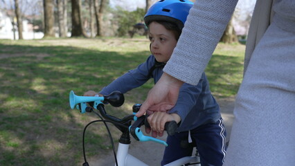 Fototapeta na wymiar Little boy learning to ride bicycle with mother support. Mom helping child to ride bike outdoors