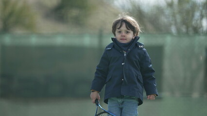 Fototapeta na wymiar Portrait little boy wearing coat during autumn season holding tennis racket outdoors