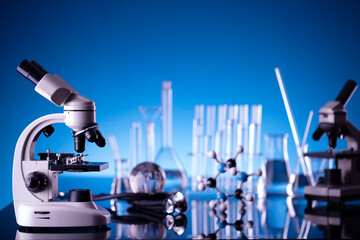 Laboratory investigations concerning test and medicine against covid. Glass tubes, microscope and beakers on blue bokeh background.