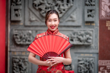 Portrait beautiful Asian woman wearing traditional cheongsam qipao dress nice smile holding red fan in Chinese festival concept.