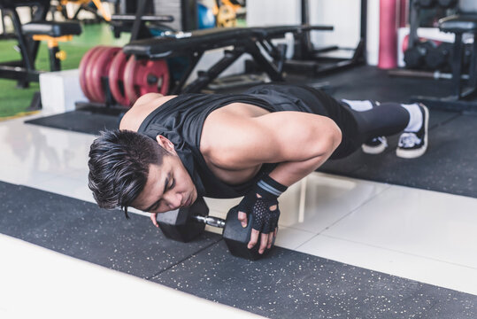 A handsome asian man does close grip pushups off of a single hex dumbbell. Chest, anterior deltoid and tricep training.