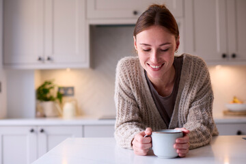 Young Woman Relaxing At Home In Kitchen Holding Hot Drink