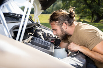 Man working inside the engine compartment of a van outdoors