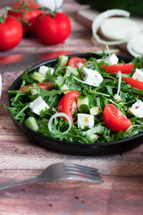Fresh spring salad with arugula, feta cheese, red onion and tomatoes in a black bowl. Recipe ingredients on chalkboard background.