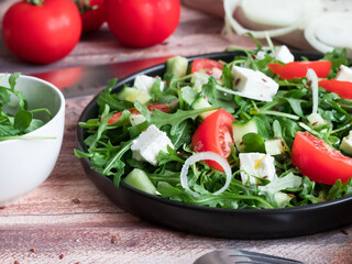 Fresh spring salad with arugula, feta cheese, red onion and tomatoes in a black bowl. Recipe ingredients on chalkboard background.