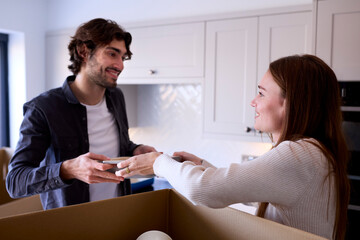 Young Couple Moving Into New Home Unpacking Boxes In Kitchen Together