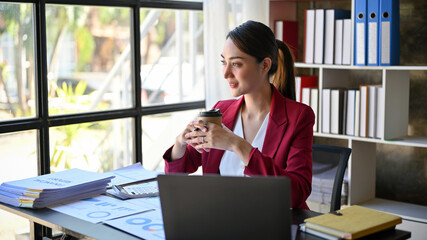 Beautiful Asian businesswoman daydreaming about her business success while sipping coffee.
