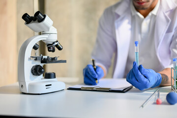 Professional Asian male scientist or chemist working in the lab, noting something on clipboard