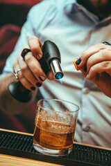Fototapeta na wymiar A bartender flaming an orange peel on a cocktail, in a bar.