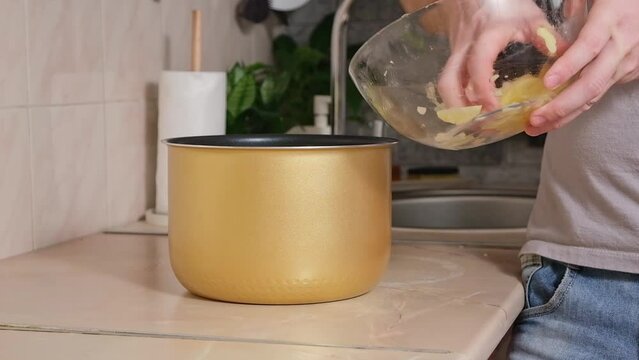 The man puts the potatoes cut into thin slices into bowl of slow cooker. multicooker. Cooking lunch dinner for family at home. The process of cooking meat in French with potatoes, tomatoes, cheese.