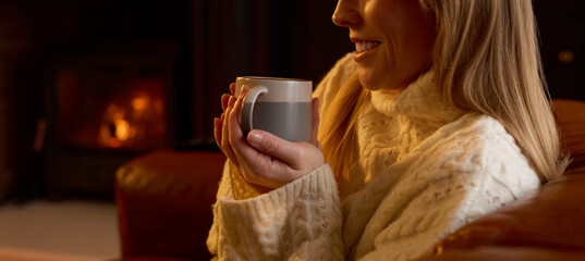 Close Up Of Woman At Home In Lounge With Cosy Fire With Hot Drink