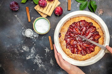Homemade plum pie. A woman cuts a plum cake with a knife, Food recipe background. Close up
