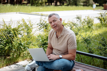 Obraz premium Expressive, charismatic senior gray haired businessman using laptop, wireless modern technology sitting on bench in park