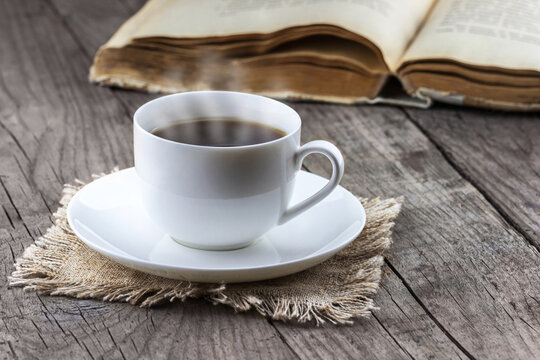 White cup of coffee with old book on wooden background
