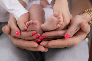 young unrecognizable family of mother father and child. Mom, dad and kid hold legs, foot of newborn baby 