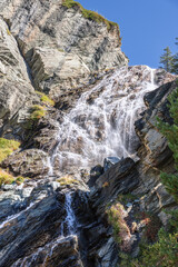 Multi-level alpine streams of Lillaz waterfall (Cascate di Lillaz) wash around granite karst rapids of rock under blue sky. Aosta valley, Italy (vertical shot)