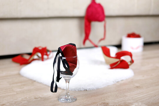 Wine glass with female thong panties, removed red bra and shoes on a floor near bed. Sex concept, romantic night of passion, sexy lingerie
