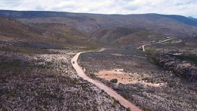 Tracking Shot flying forward turning right over a  a curvy dirt road at a dessert valley in Cloetesberg,  on edge of the klein karoo semi desert region and garden routes, Western Cape, South Africa.