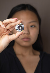 Young Asian woman evaluates a round cut diamond through a magnifying glass close up. High quality photo